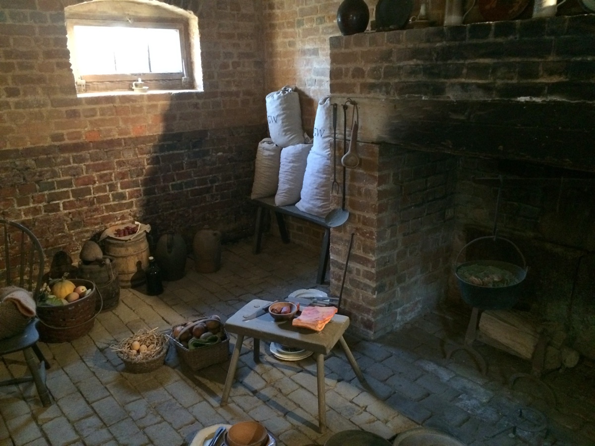 A preserved brick kitchen with a hearth, baskets, and period tools
