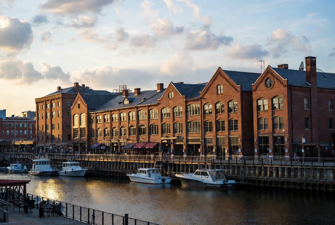 Historic brick warehouse buildings along a waterfront with boats moored at golden hour